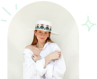 Brittany Merrill wearing white oversized shirt, white wide-brimmed hat with boho patterned trim & gold chain jewelry